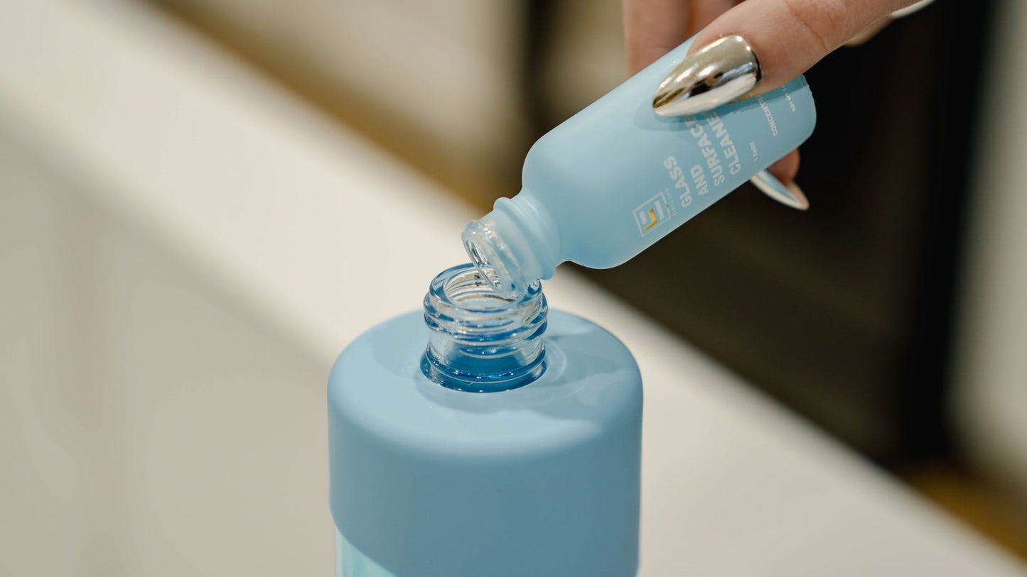 Pouring ESNTL LVG concentrated glass and surface cleaner into a reusable bottle, promoting zero waste and sustainable cleaning solutions.