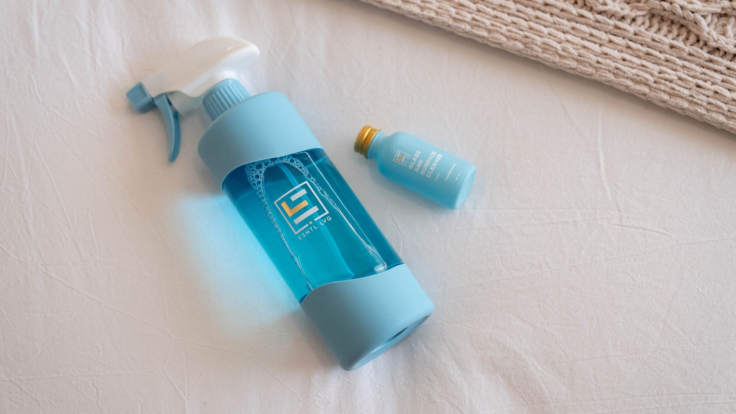 Reusable ESNTL LVG glass spray bottle with blue cleaning solution and a refillable concentrate bottle, promoting sustainable, plastic-free cleaning alternatives.
