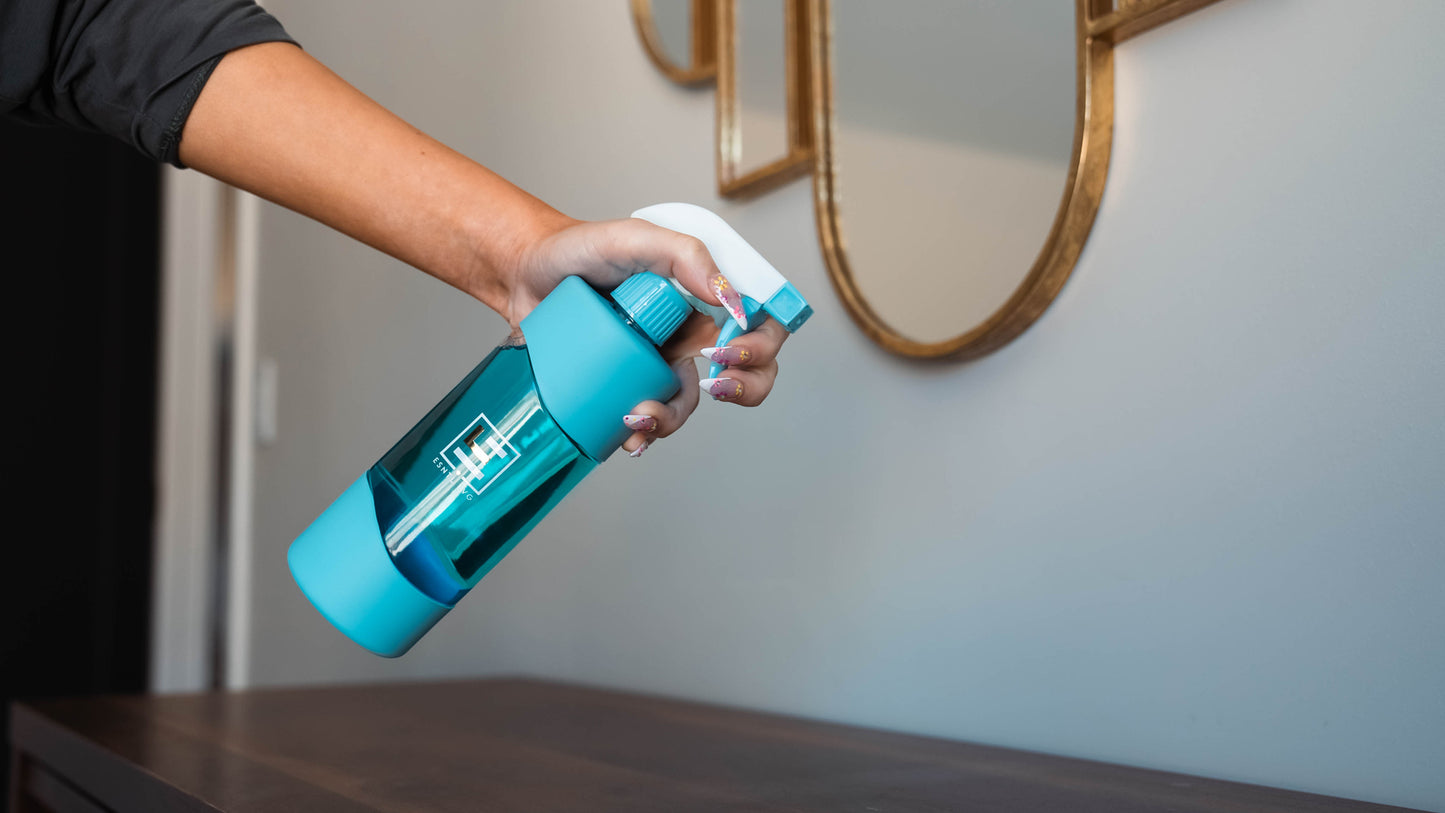 Person holding blue reusable glass spray bottle from ESNTL LVG filled with eco friendly cleaner