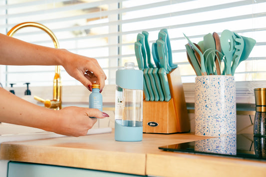 A person pouring a glass and surface cleaner concentrate into a reusable glass spray bottle in a modern kitchen with eco-friendly utensils and decor.