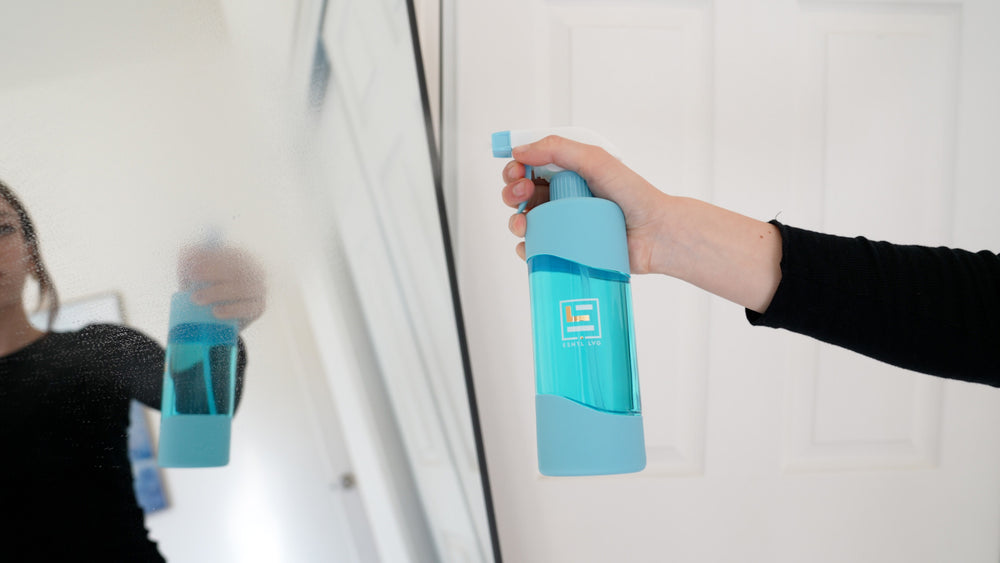 Image of person using esntl lvg sustainable glass and surface cleaner with blue glass reusable bottle