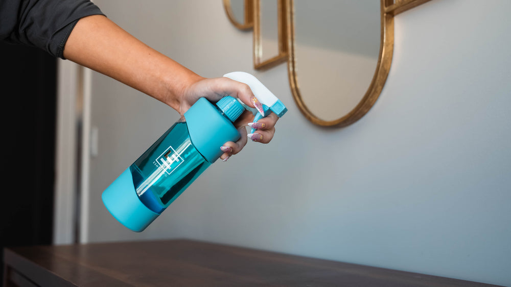 Person holding blue reusable glass spray bottle from ESNTL LVG filled with eco friendly cleaner