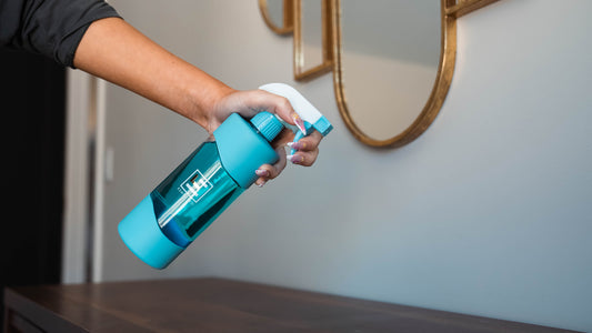 Person holding blue reusable glass spray bottle from ESNTL LVG filled with eco friendly cleaner